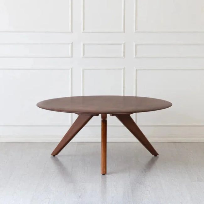 Sora round solid wood coffee table on three splayed legs against a white panelled wall