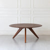 Sora round solid wood coffee table on three splayed legs against a white panelled wall