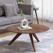 Sora round wooden coffee table with a white vase in front of a grey sofa