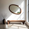 Wave Oval Walnut Wood Wall Mirror above a wooden bench with a vase